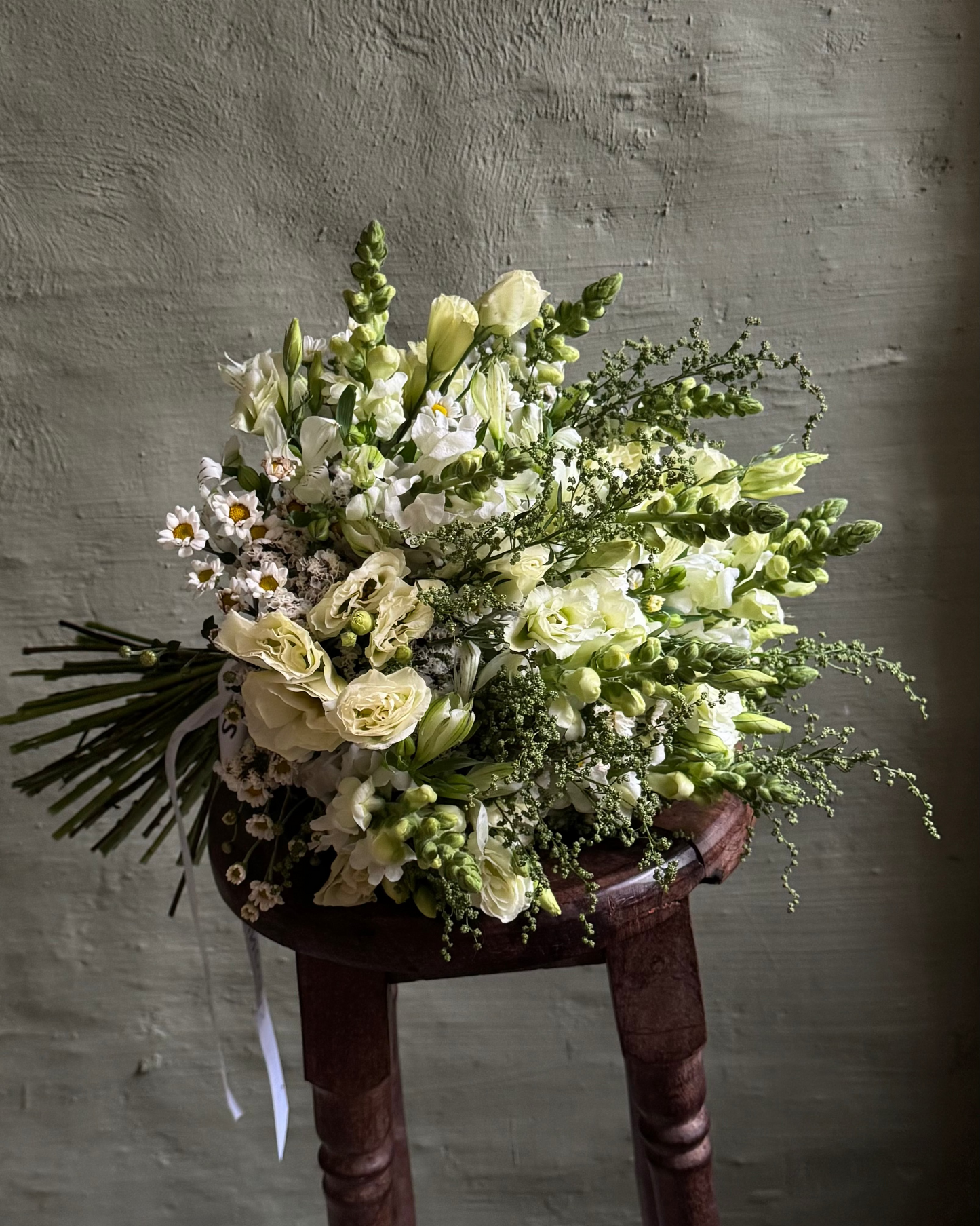 Bouquet of flowers on a wooden stool against a textured wall.