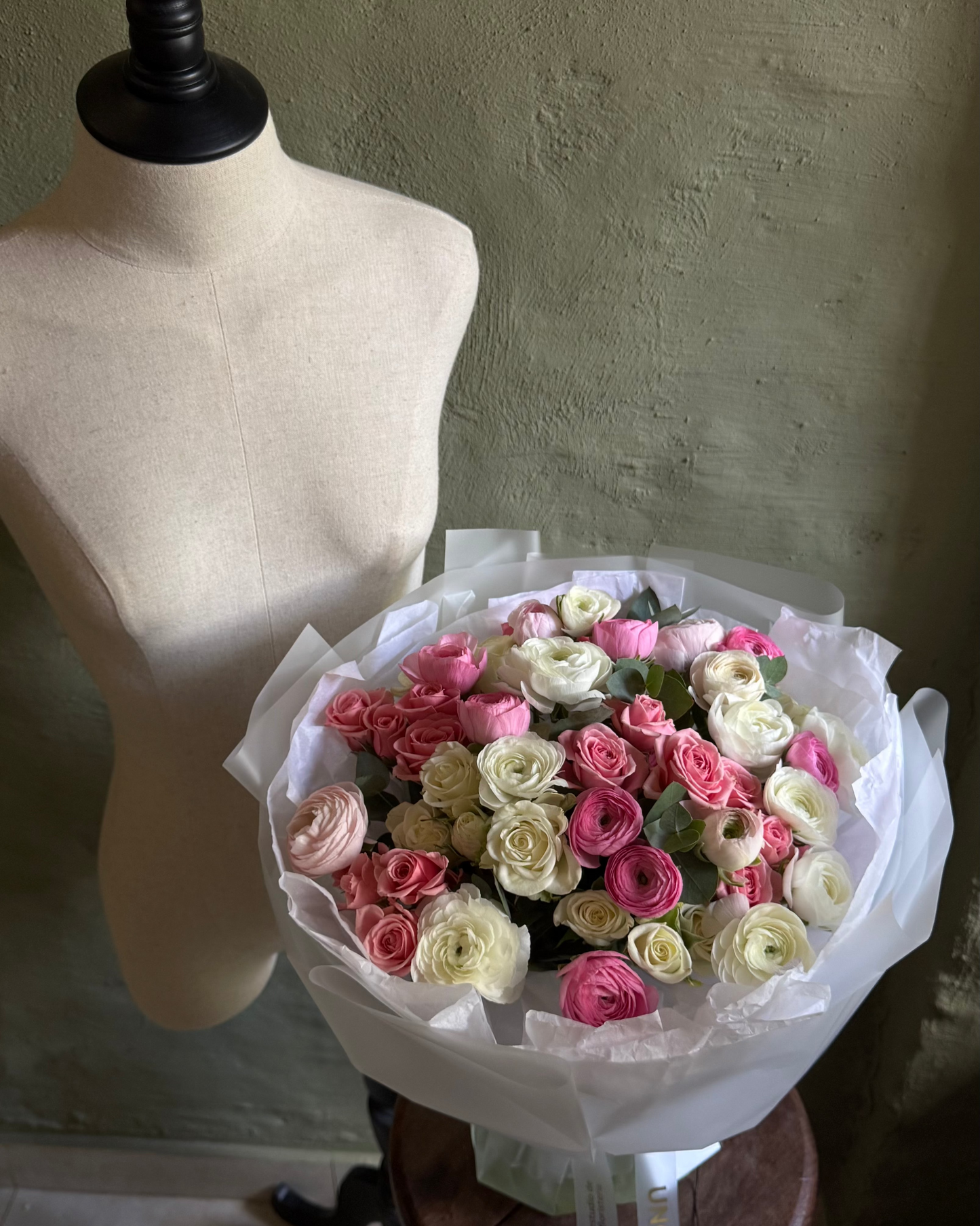 Bouquet of pink and white flowers on a mannequin stand against a plain wall.