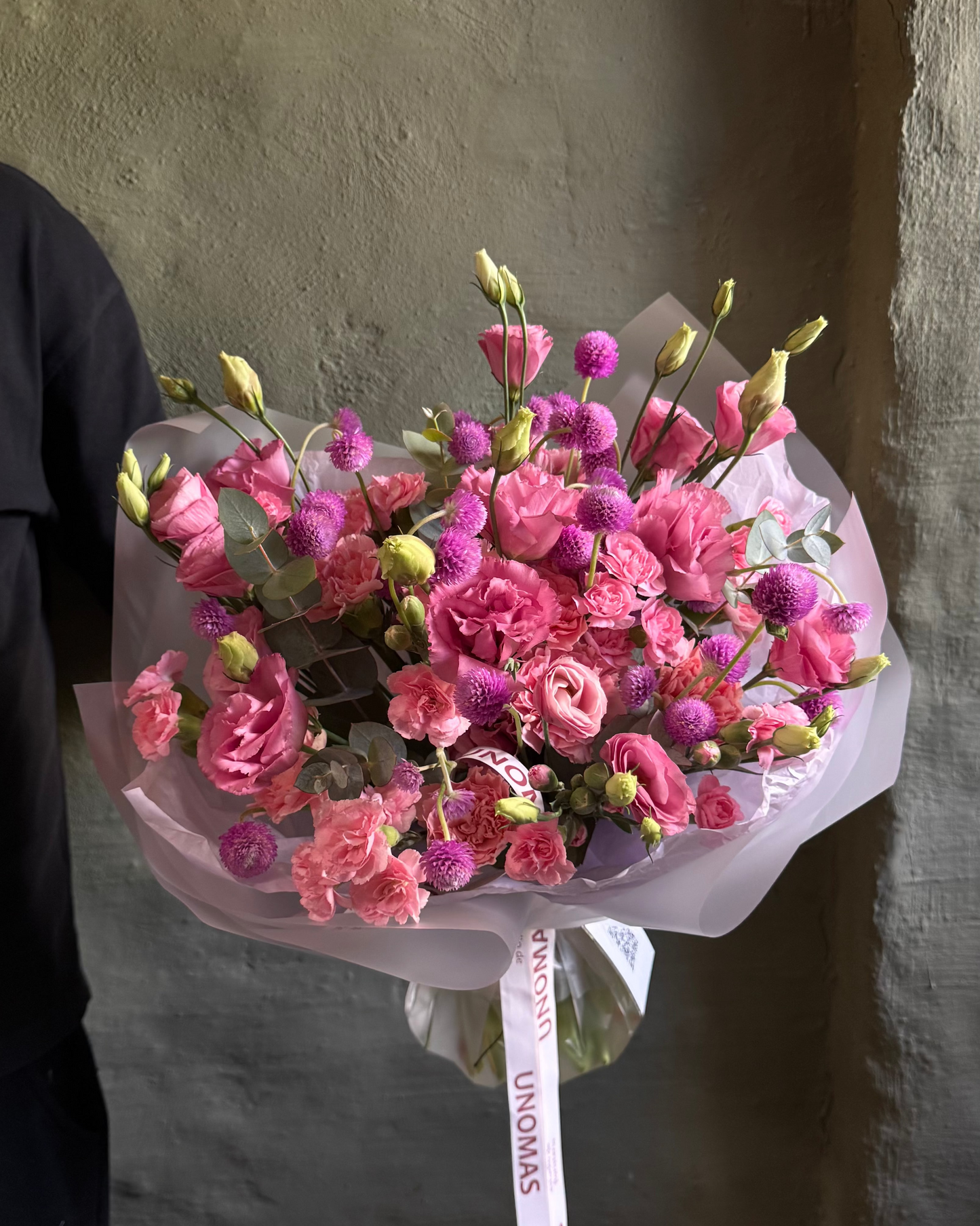 Bouquet of pink flowers with green leaves held against a plain background