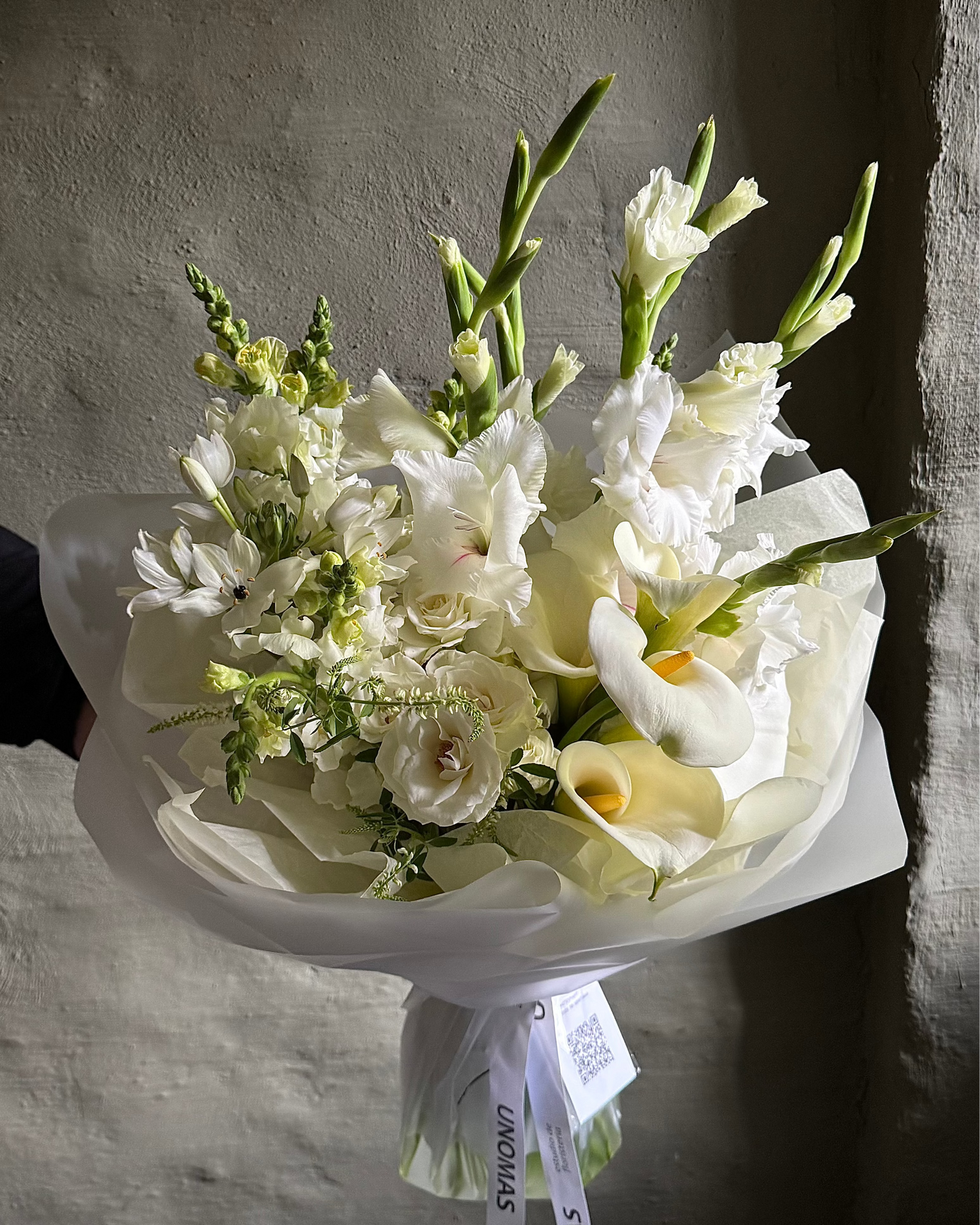 Bouquet of white flowers with green stems held against a plain background