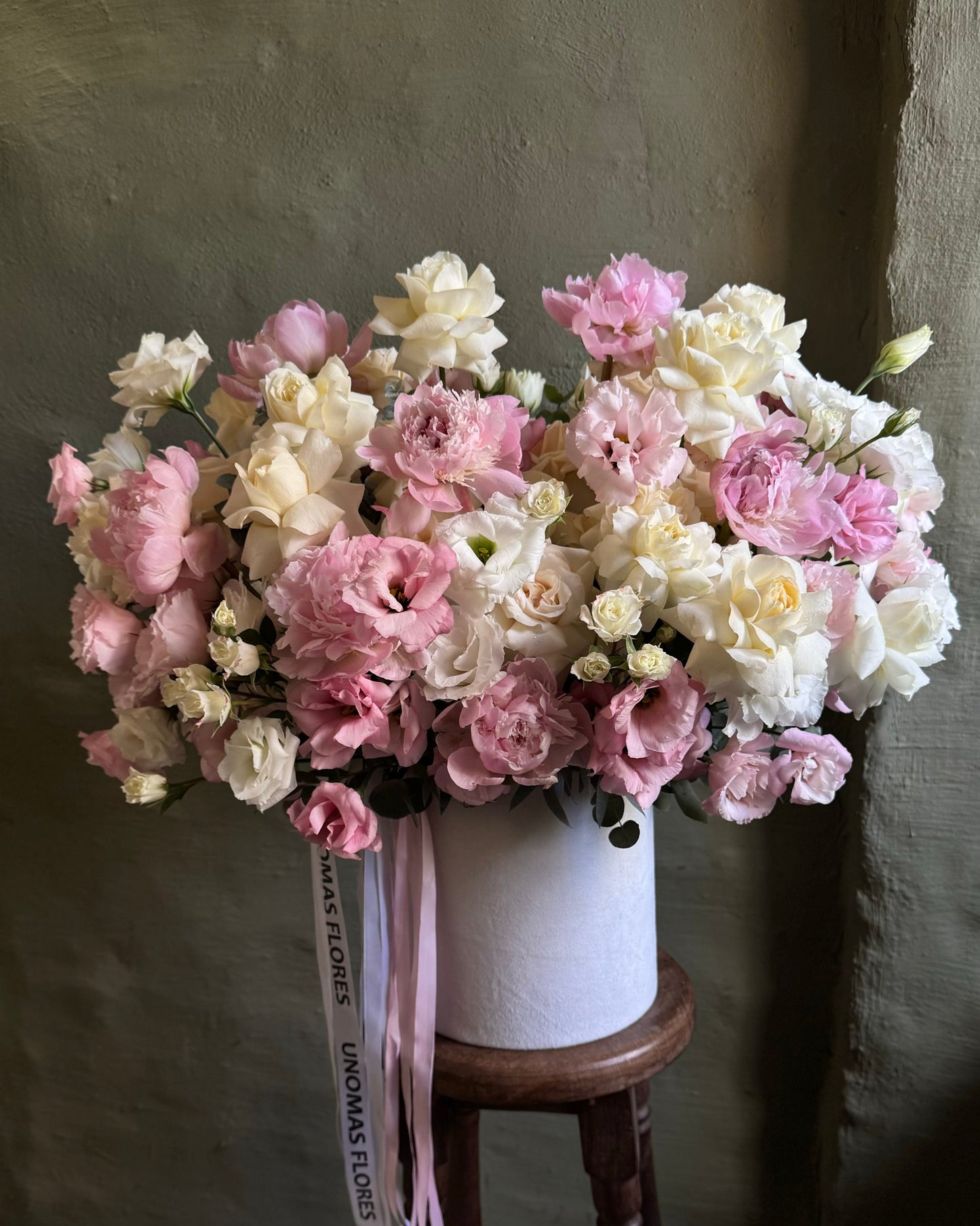 Bouquet of pink and white flowers in a white vase on a wooden stool against a gray wall.