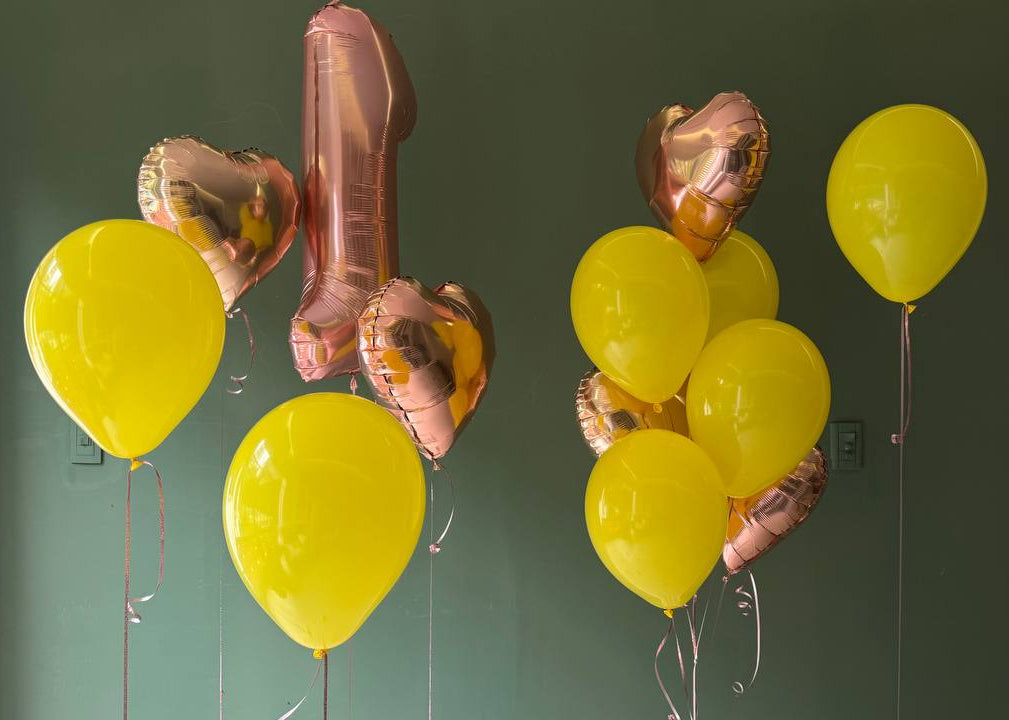 Gold number '1' balloon and yellow balloons against a green wall