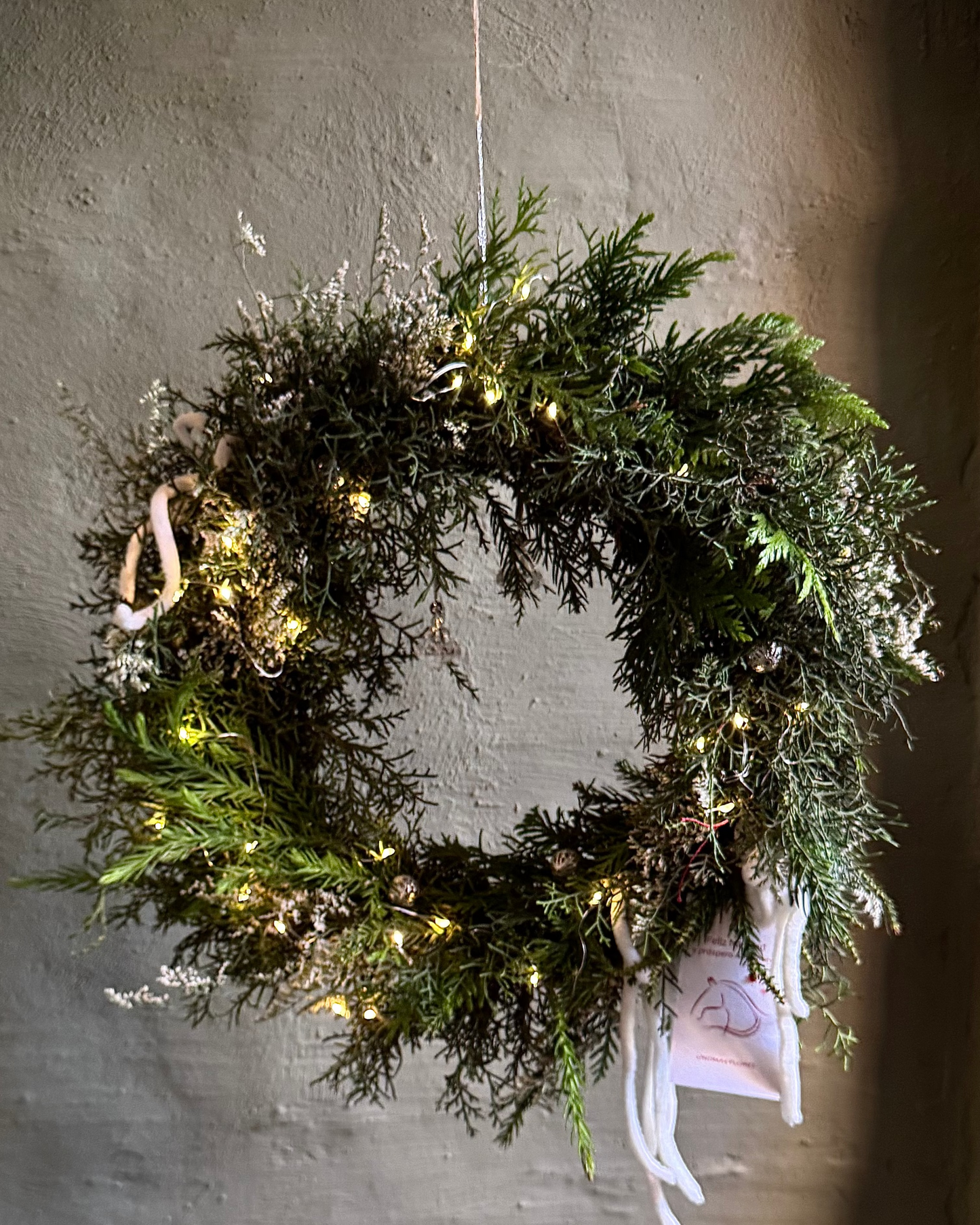 Green wreath with lights and ribbons hanging on a textured wall
