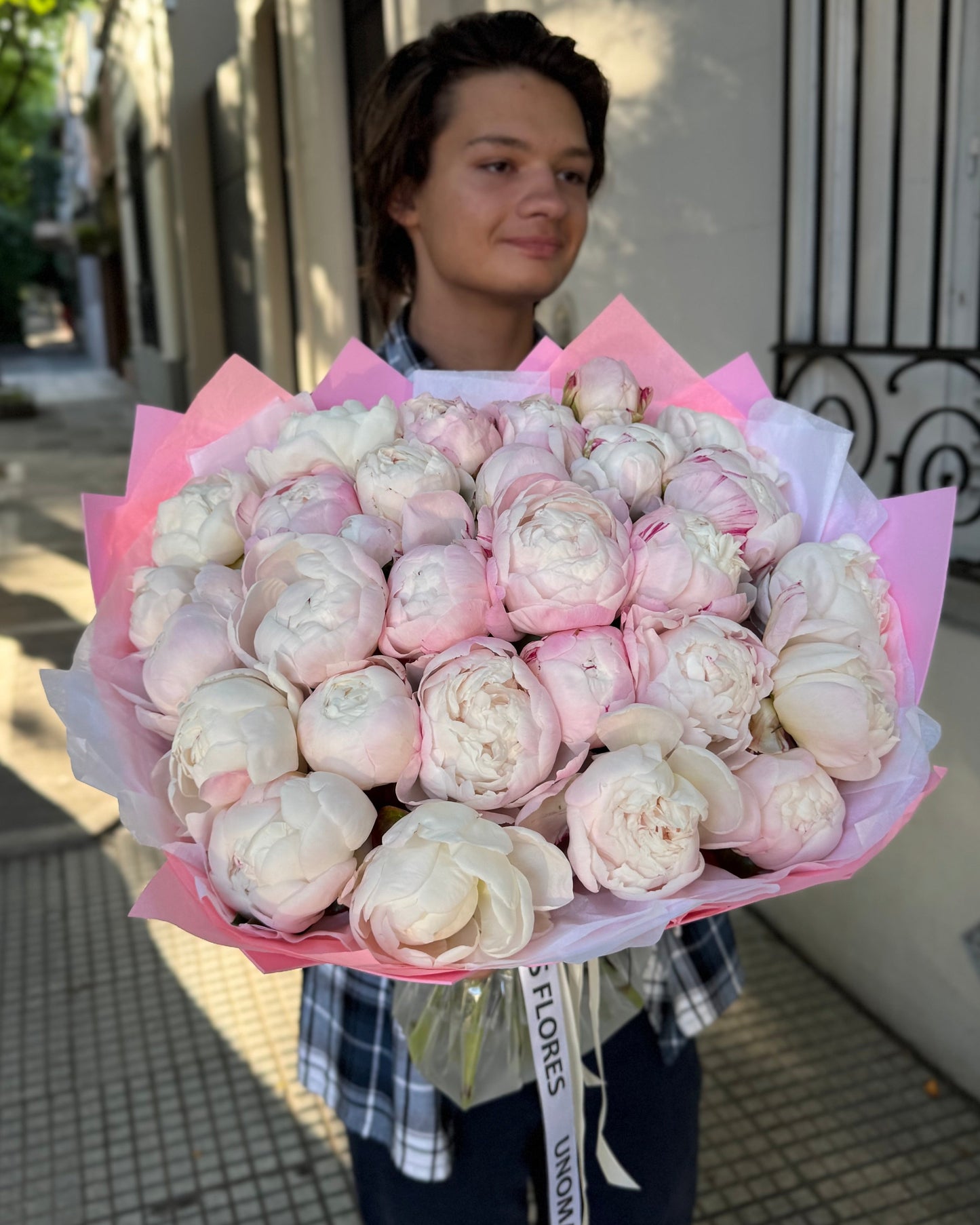 Person holding a large bouquet of white and pink flowers outdoors.