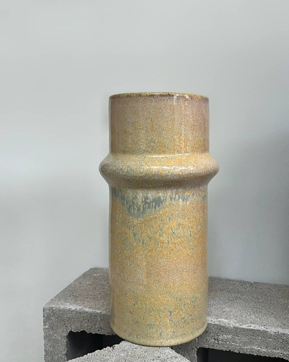 Cylindrical ceramic vase with textured surface on a gray surface against a white background