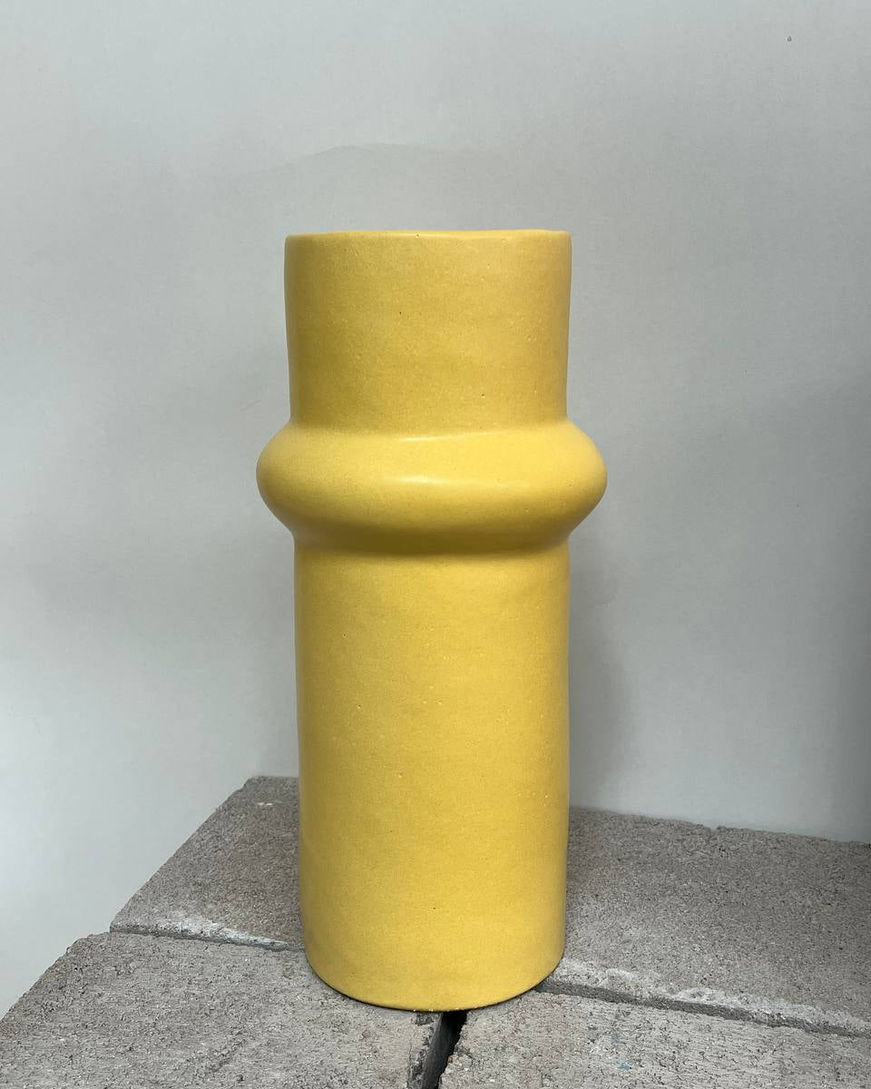 Yellow cylindrical vase on a gray surface with a light gray background