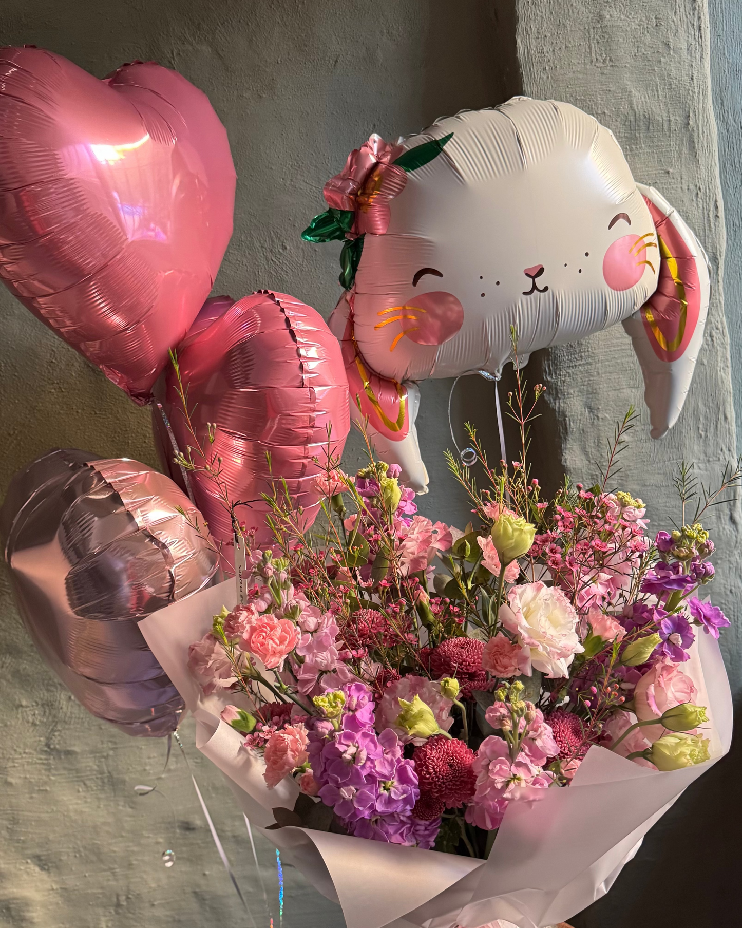 Bouquet of flowers with a rabbit-shaped balloon and heart-shaped balloons on a concrete surface.
