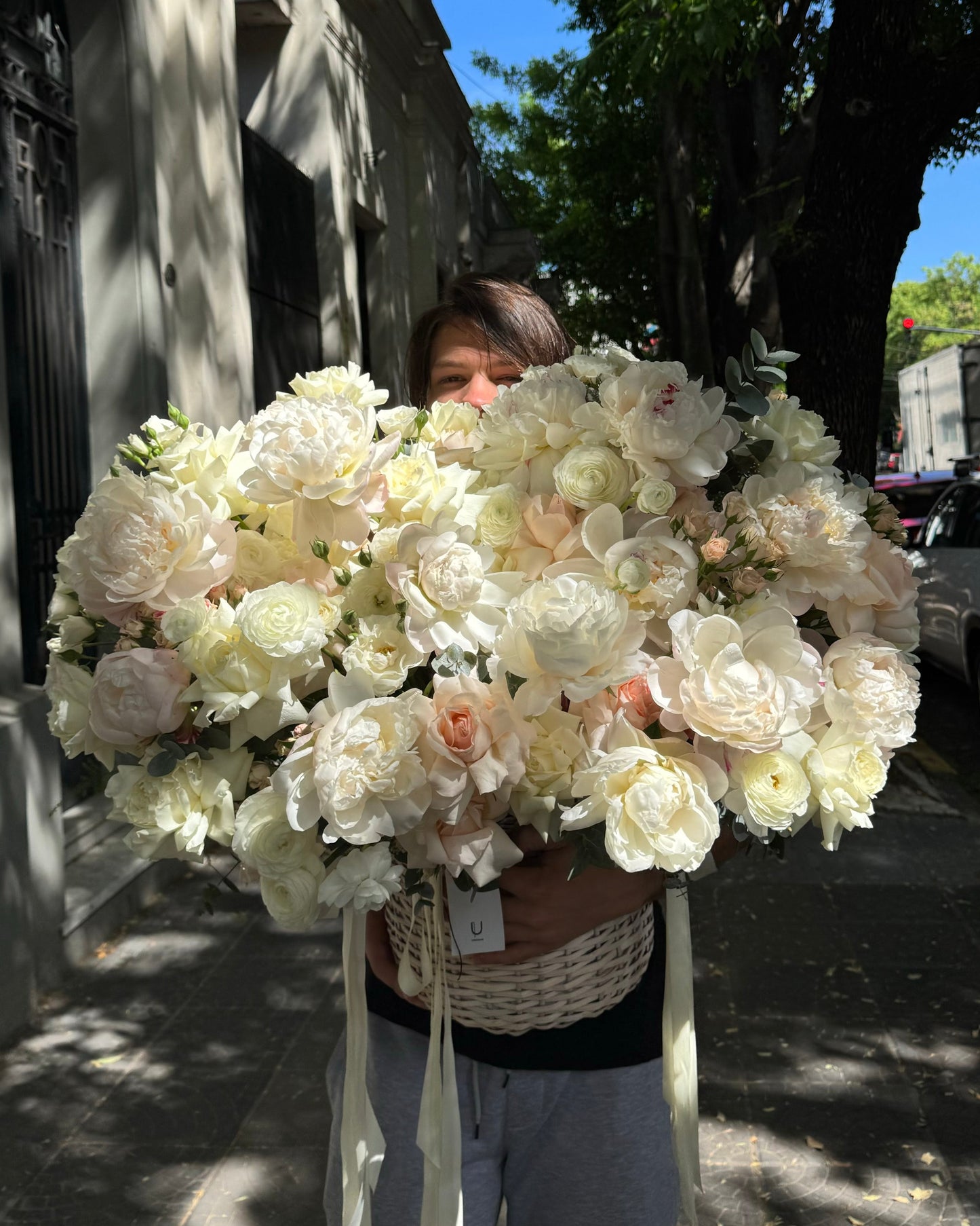 Person holding a large bouquet of white flowers peonies outdoors.