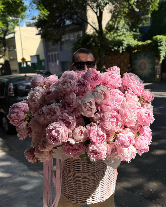Person holding a large bouquet of pink flowers outdoors on a street.