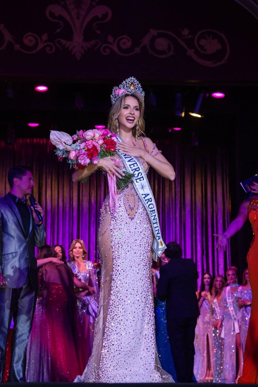 Miss Universe Argentina winner holding a bouquet on a stage with other people.