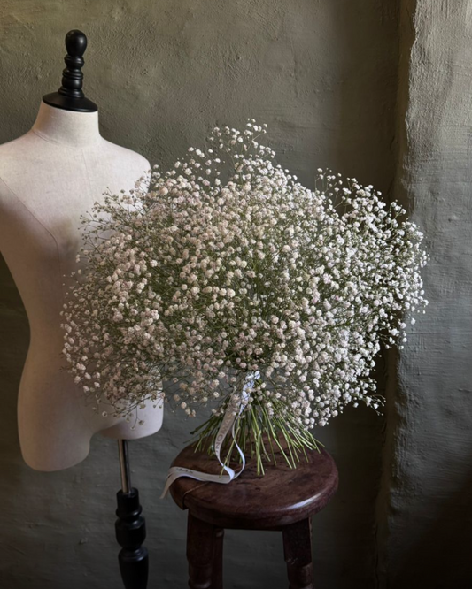 Bouquet of baby's breath on a wooden stool next to a mannequin against a textured wall.