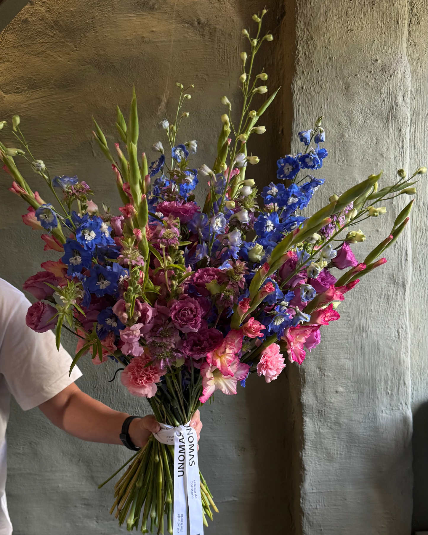Bouquet of colorful flowers held by a person against a textured wall.