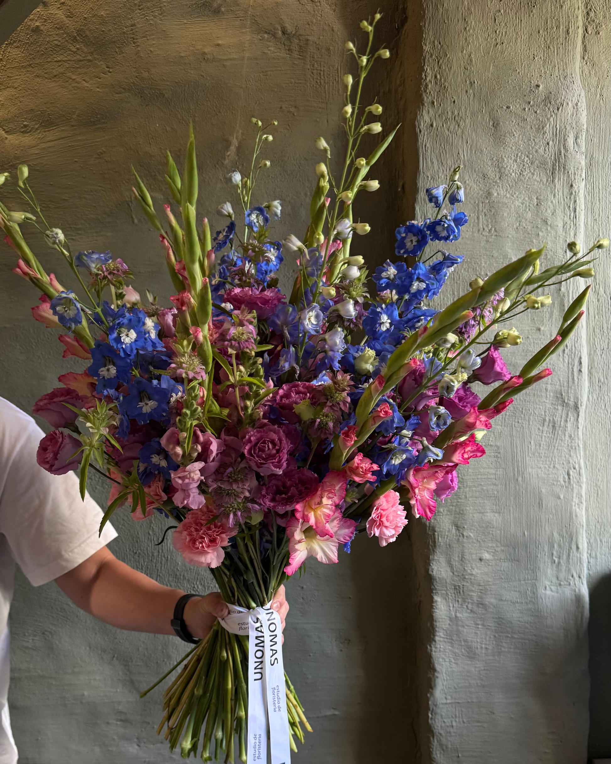 Bouquet of colorful flowers held by a person against a textured wall.