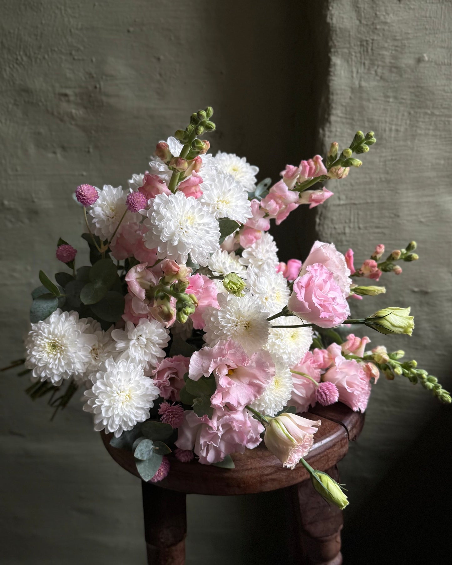 Bouquet of flowers on a wooden stool against a textured wall.