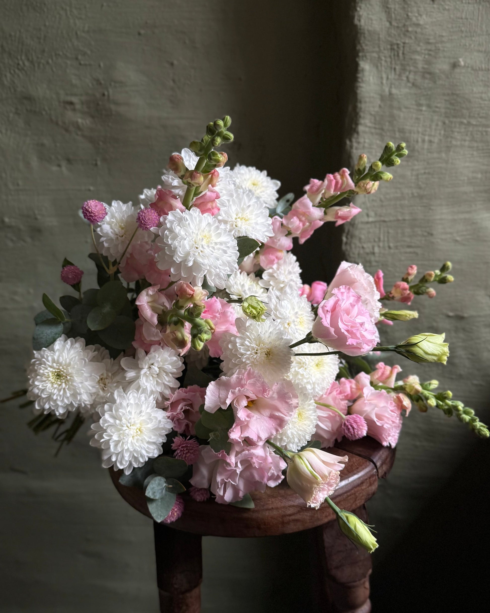 Bouquet of flowers on a wooden stool against a textured wall.