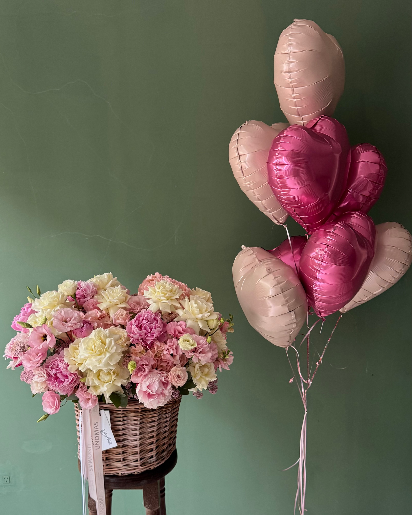 Bouquet of flowers on a wooden stool with heart-shaped balloons against a green wall.