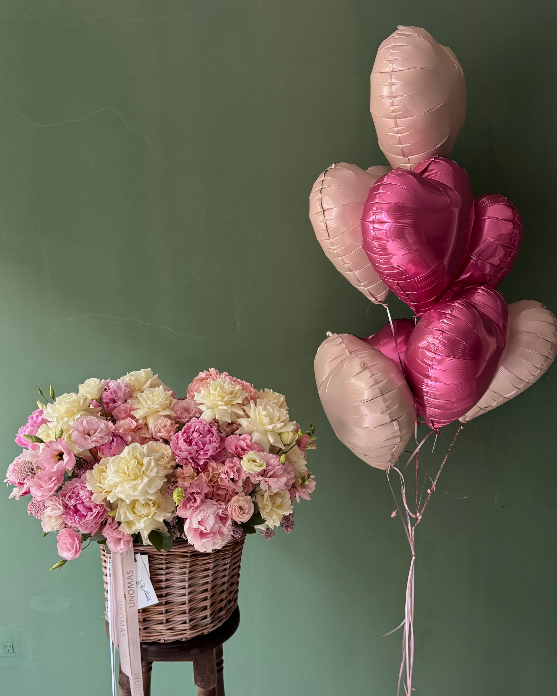 Bouquet of flowers on a wooden stool with heart-shaped balloons against a green wall.