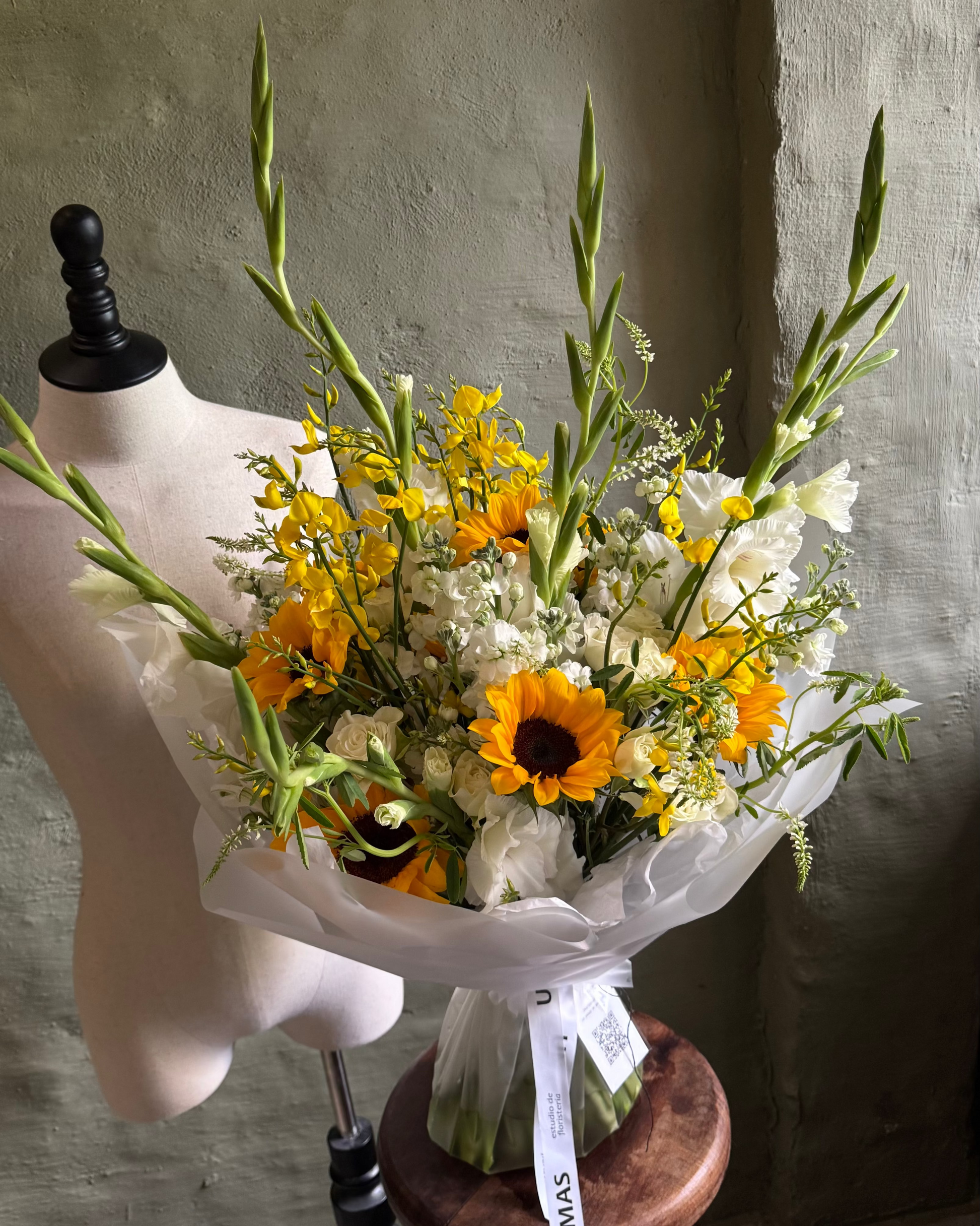 Bouquet of flowers on a mannequin with a wooden stool against a textured wall.