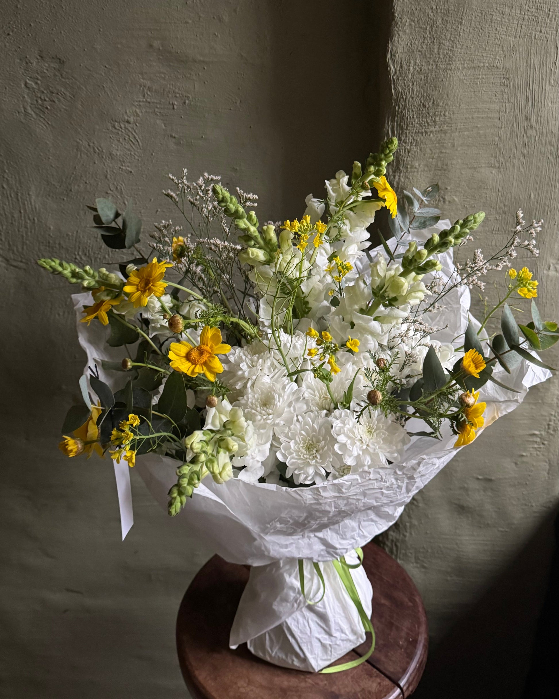 Bouquet of flowers on a wooden stool against a textured wall.
