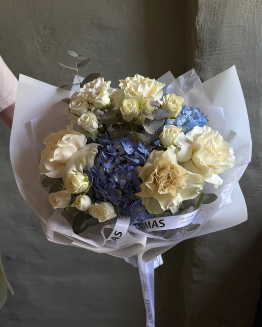 Bouquet of flowers with white and blue flowers wrapped in paper against a plain background