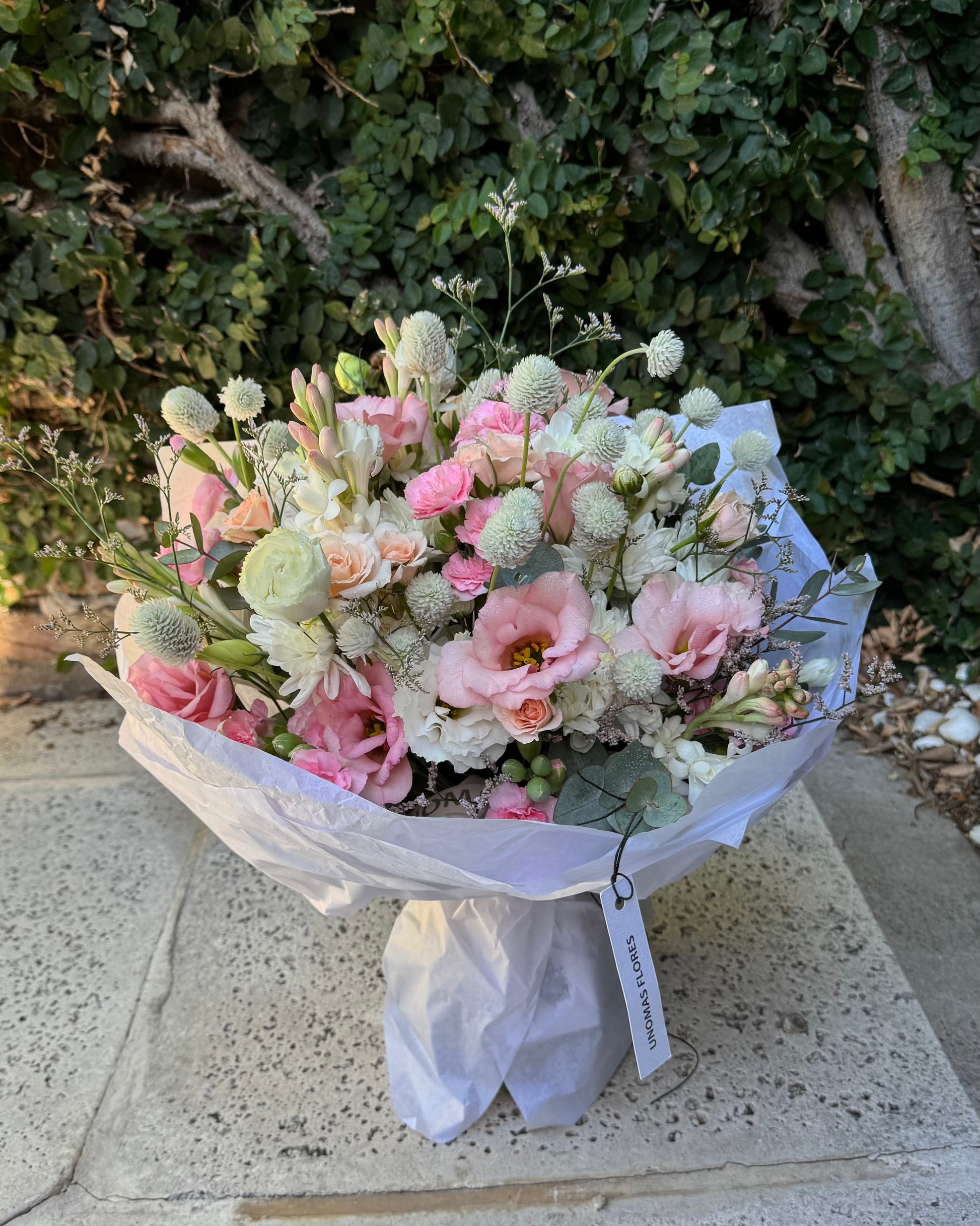 Bouquet of flowers wrapped in white paper on a stone surface with greenery in the background