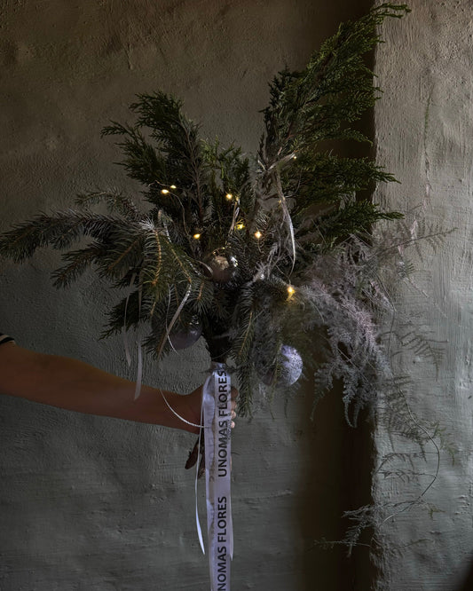 Bouquet of greenery with lights held against a textured wall.