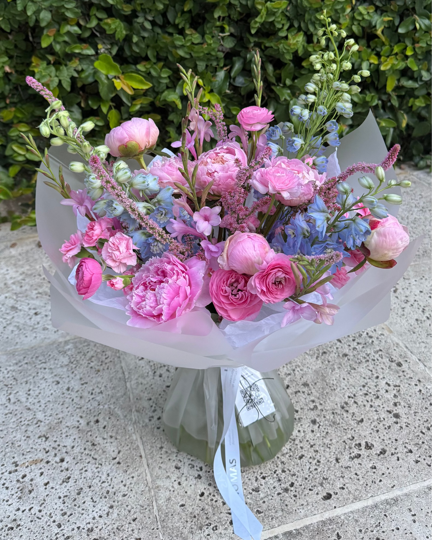 Bouquet of pink and blue flowers peonies on a stone surface with greenery in the background