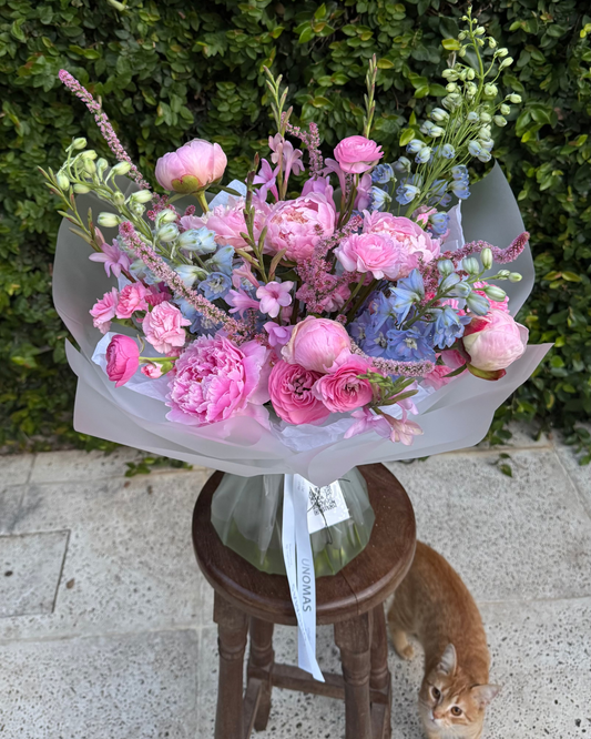 Bouquet of pink and blue peony flowers on a wooden stool with a green bush background