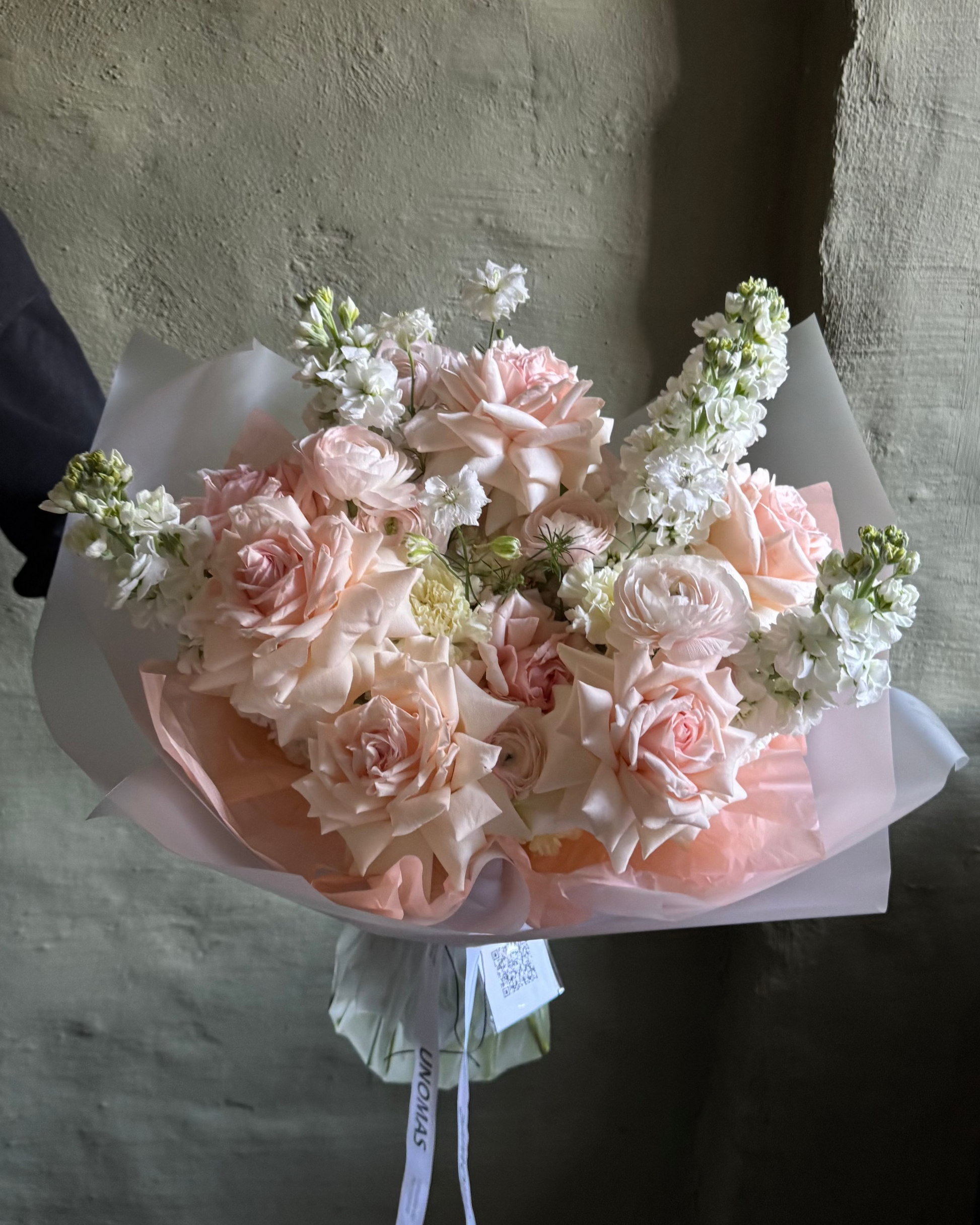 Bouquet of pink and white flowers held against a textured wall.