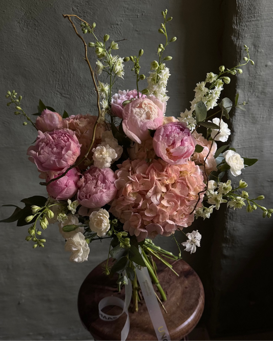Bouquet of pink and white flowers on a wooden stool against a gray wall.