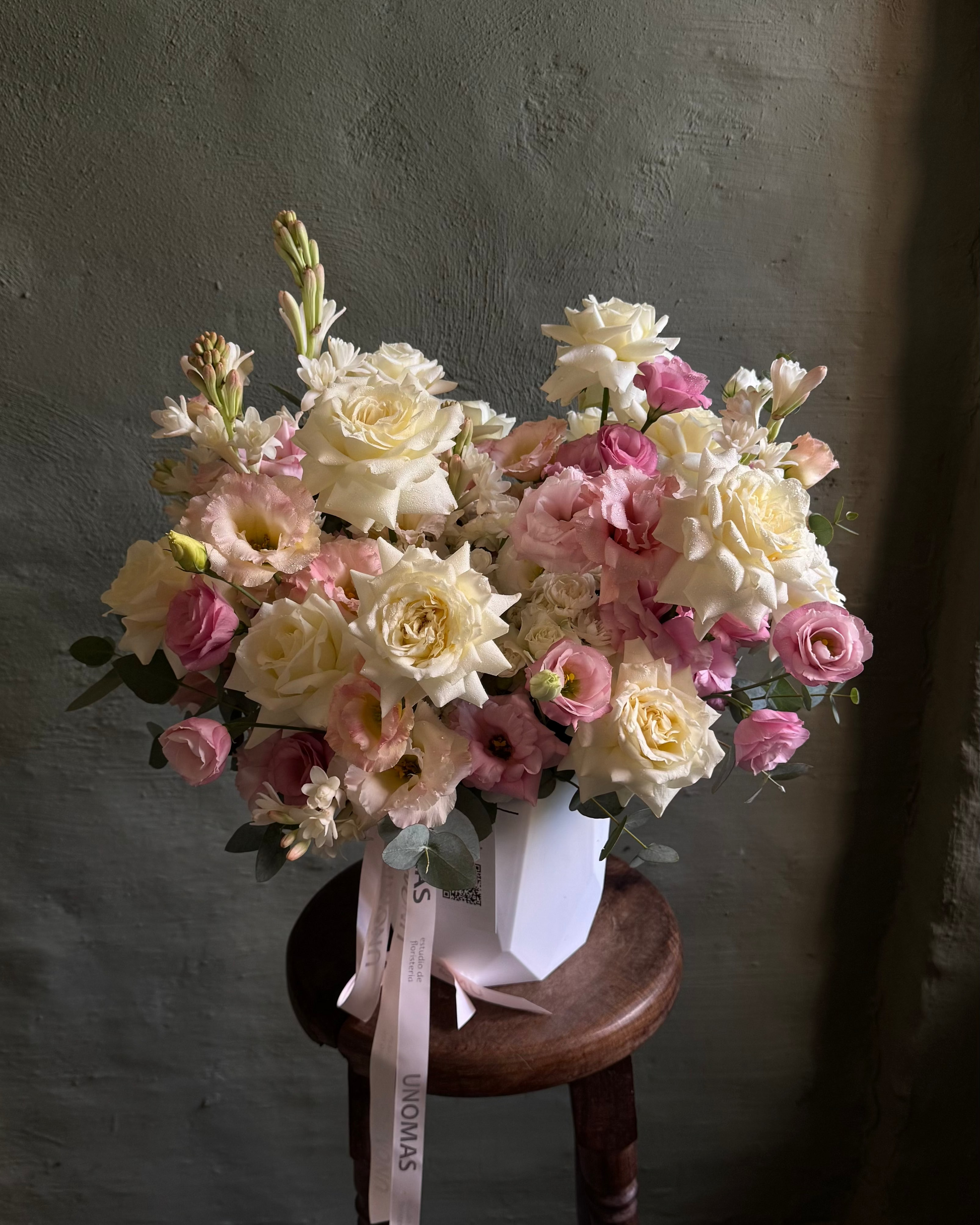 Bouquet of pink and white flowers on a wooden stool against a gray wall.