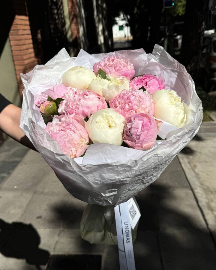 Bouquet of pink and white flowers wrapped in paper with a visible brand name.