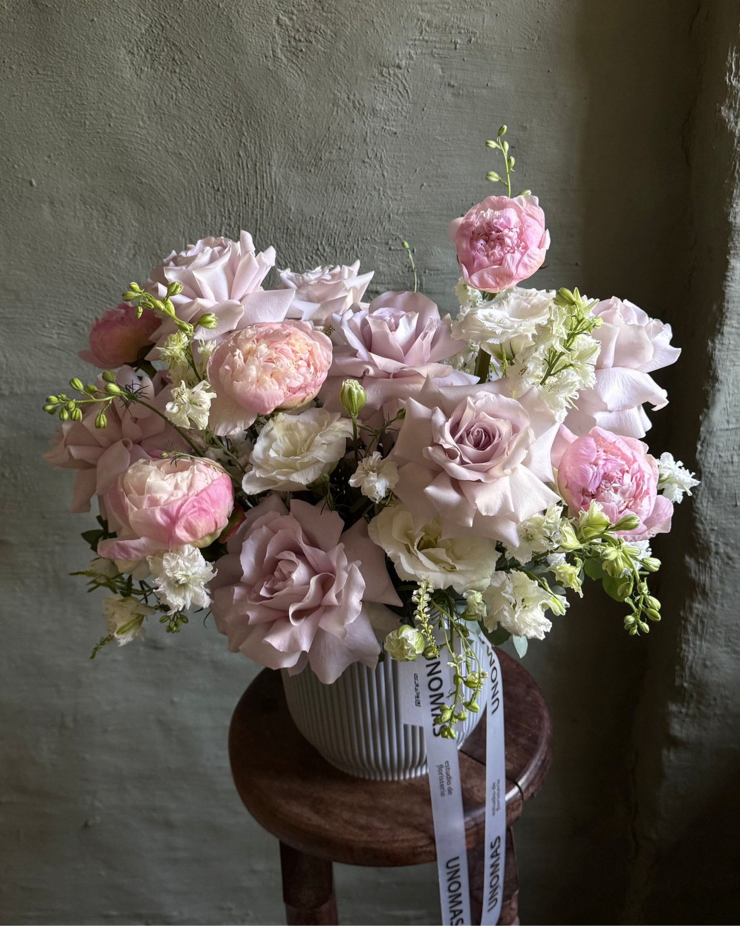 Bouquet of pink and white flowers on a wooden stool against a textured wall.
