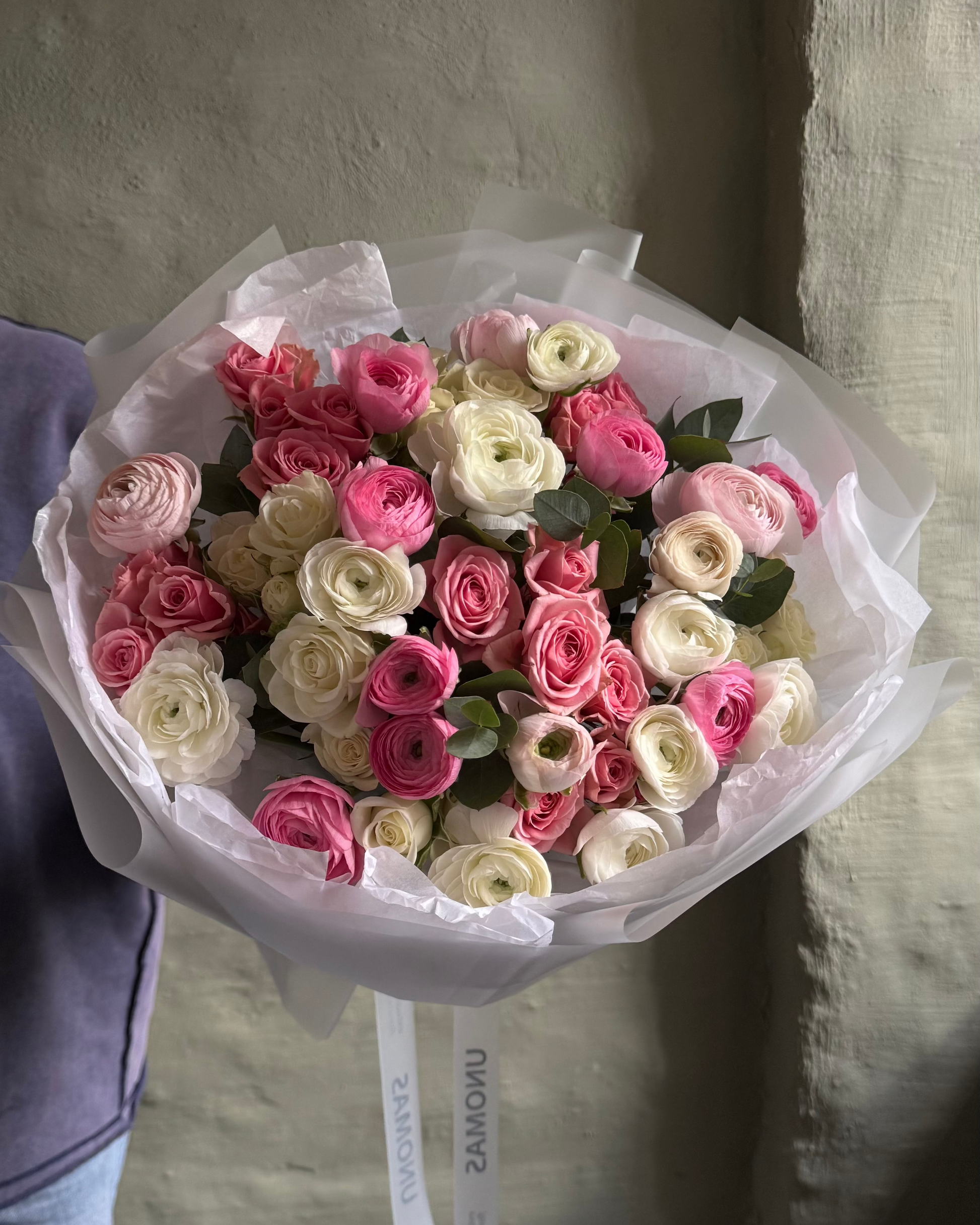 Bouquet of pink and white flowers with ranunculus and spray roses gift wrapped  against a neutral background.