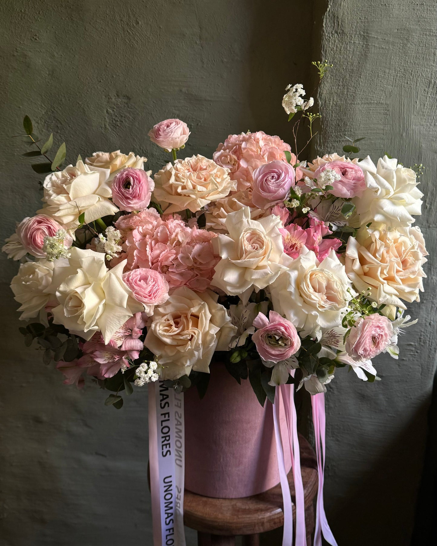 Bouquet of pink and white flowers with ribbons on a wooden stool against a plain background