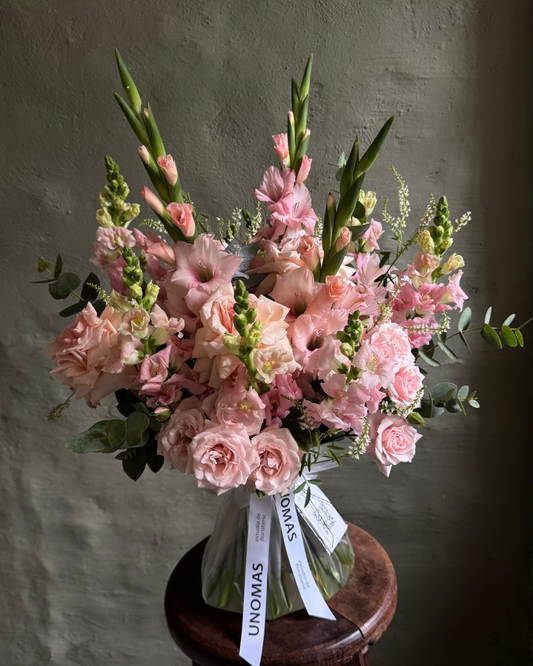 Bouquet of pink flowers gladioli anf spray roses on a wooden stool against a gray wall.