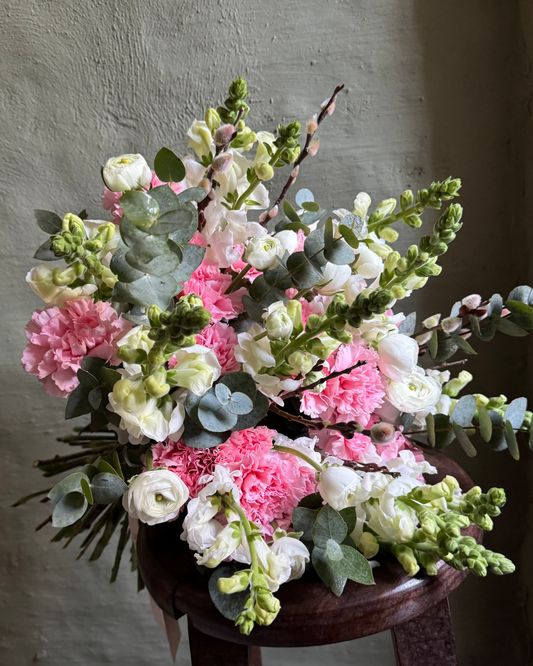 Bouquet of pink, white, and green flowers on a wooden stool against a neutral background