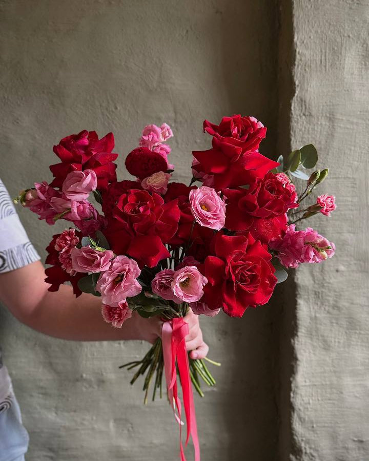Bouquet of red and pink flowers held by a person against a plain background