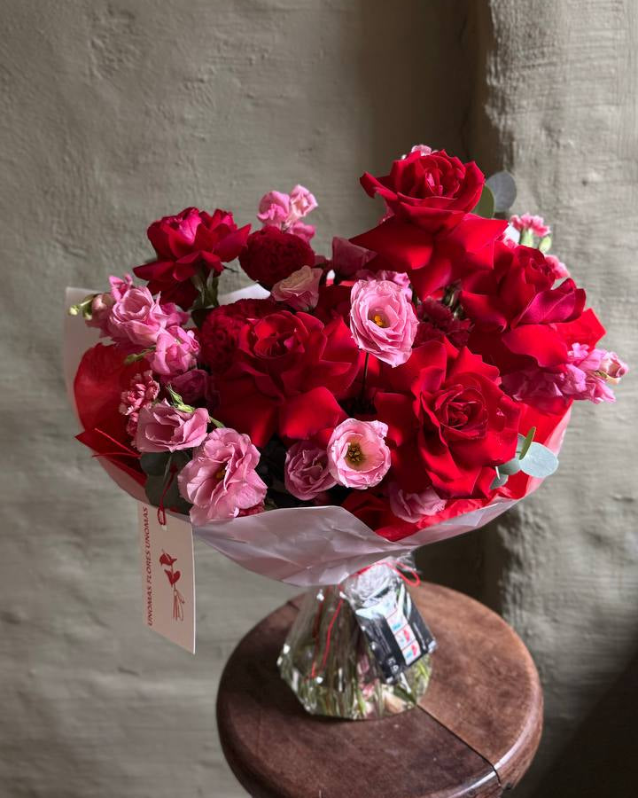 Bouquet of red and pink flowers on a wooden stool against a textured wall.