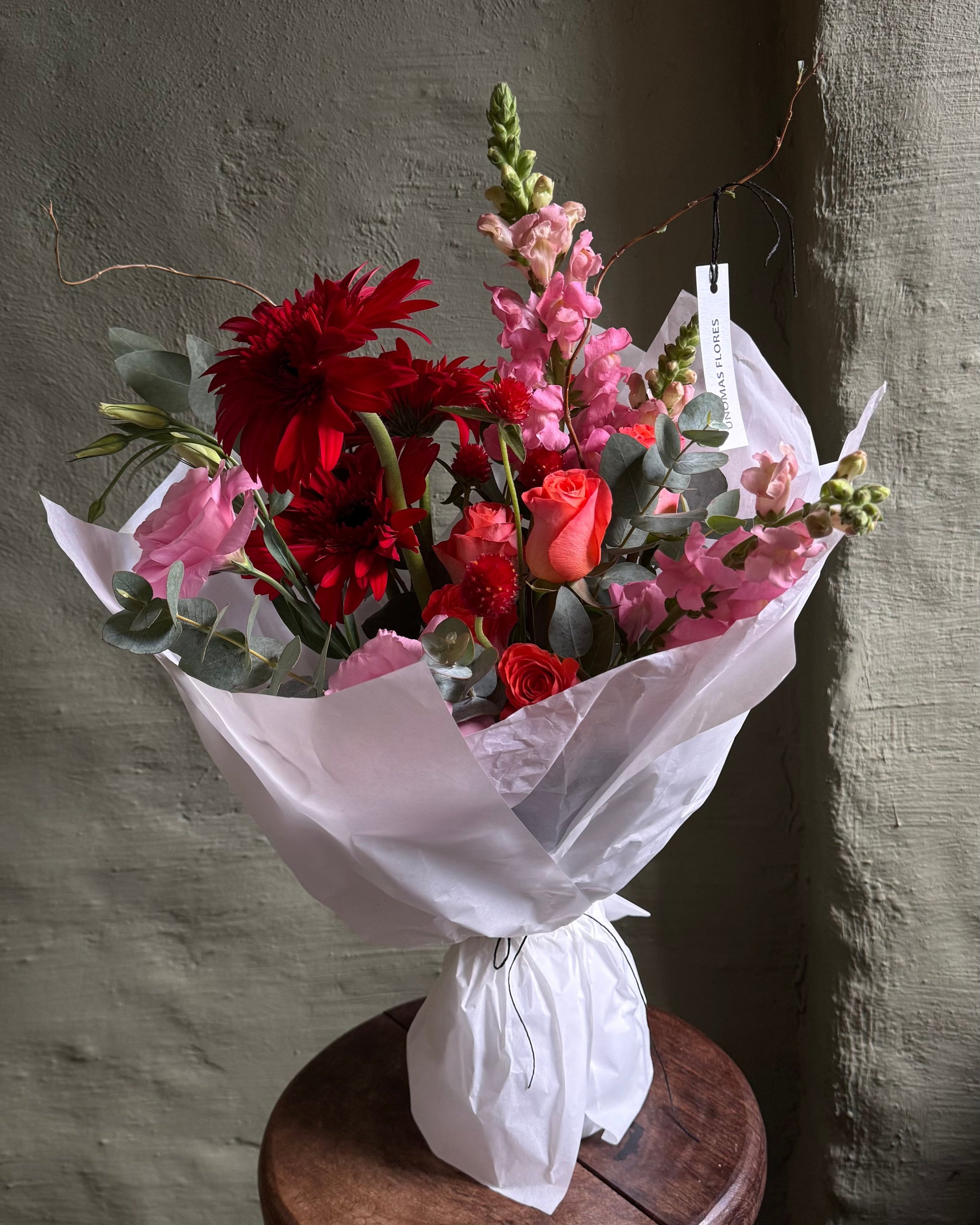 Bouquet of red and pink flowers on a wooden stool against a textured wall.