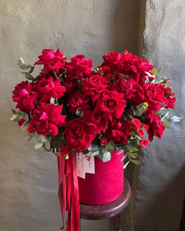 Bouquet of red flowers in a pink container on a wooden stool against a textured wall.