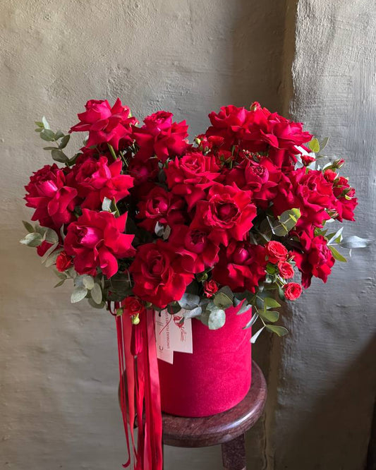 Bouquet of red flowers in a pink container on a wooden stool against a textured wall.