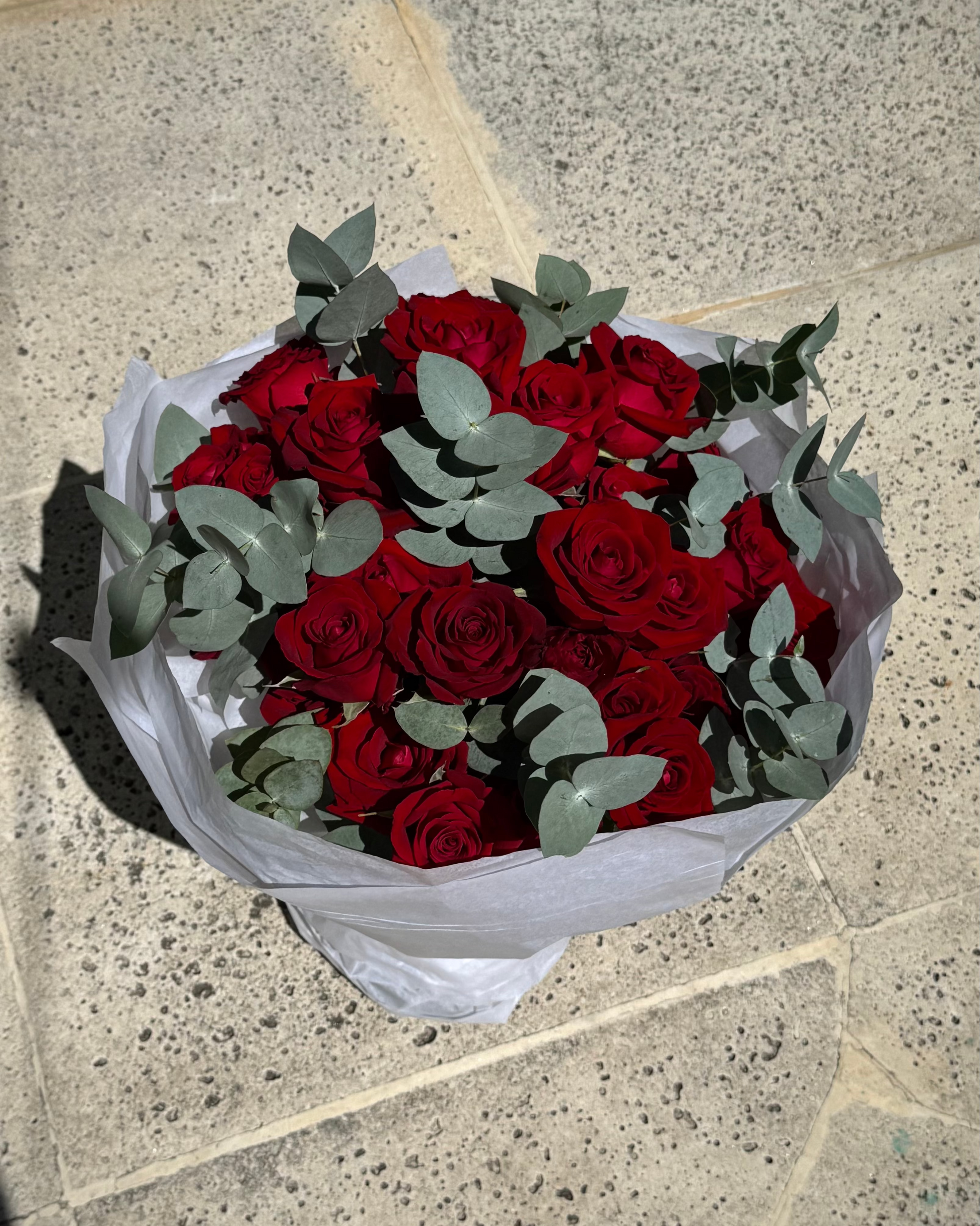 Bouquet of red roses with greenery on a stone pavement