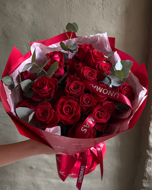 Bouquet of red roses wrapped in red paper with a visible brand logo, held against a plain background.