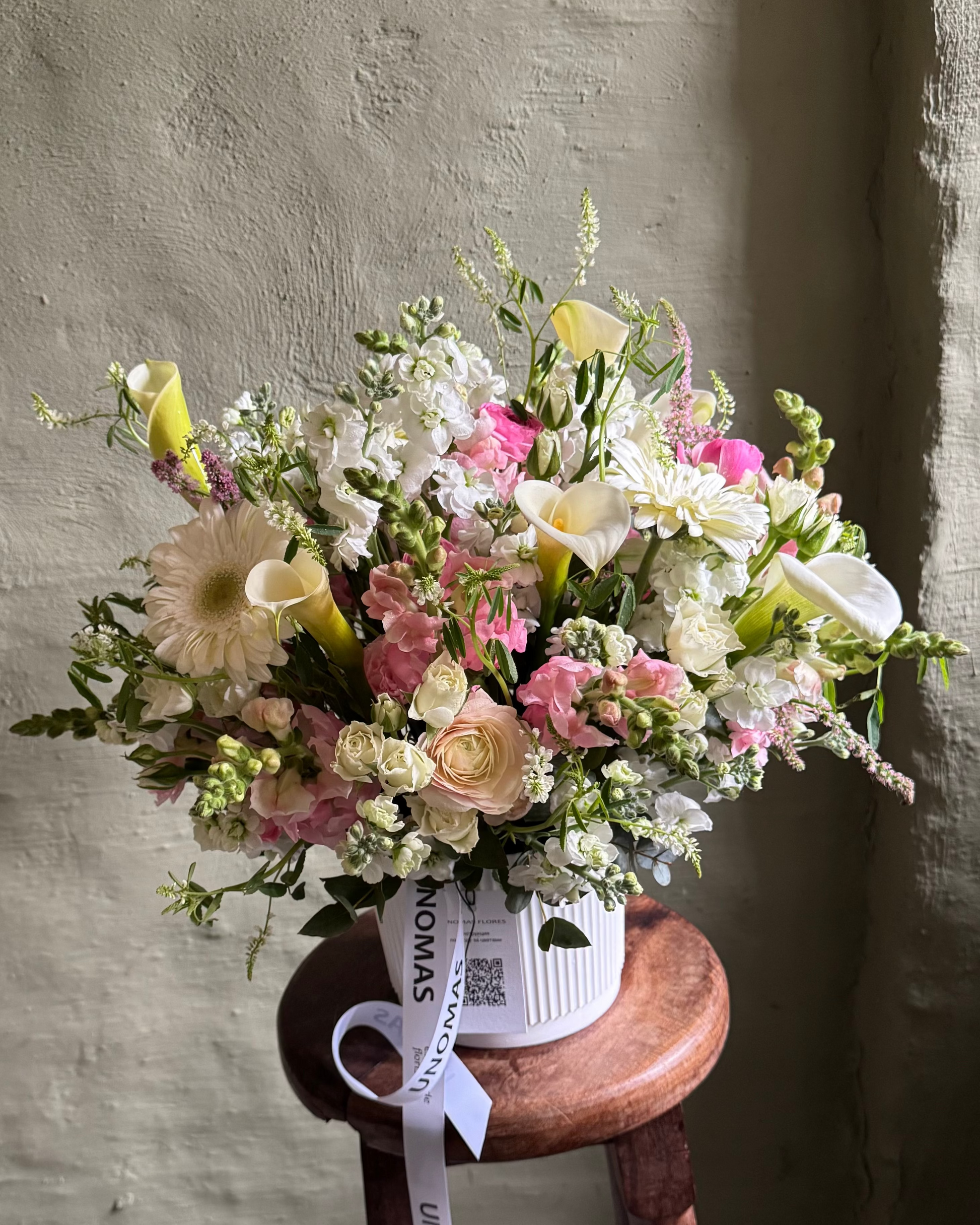 Bouquet of spring seasonal flowers on a wooden stool against a textured wall.