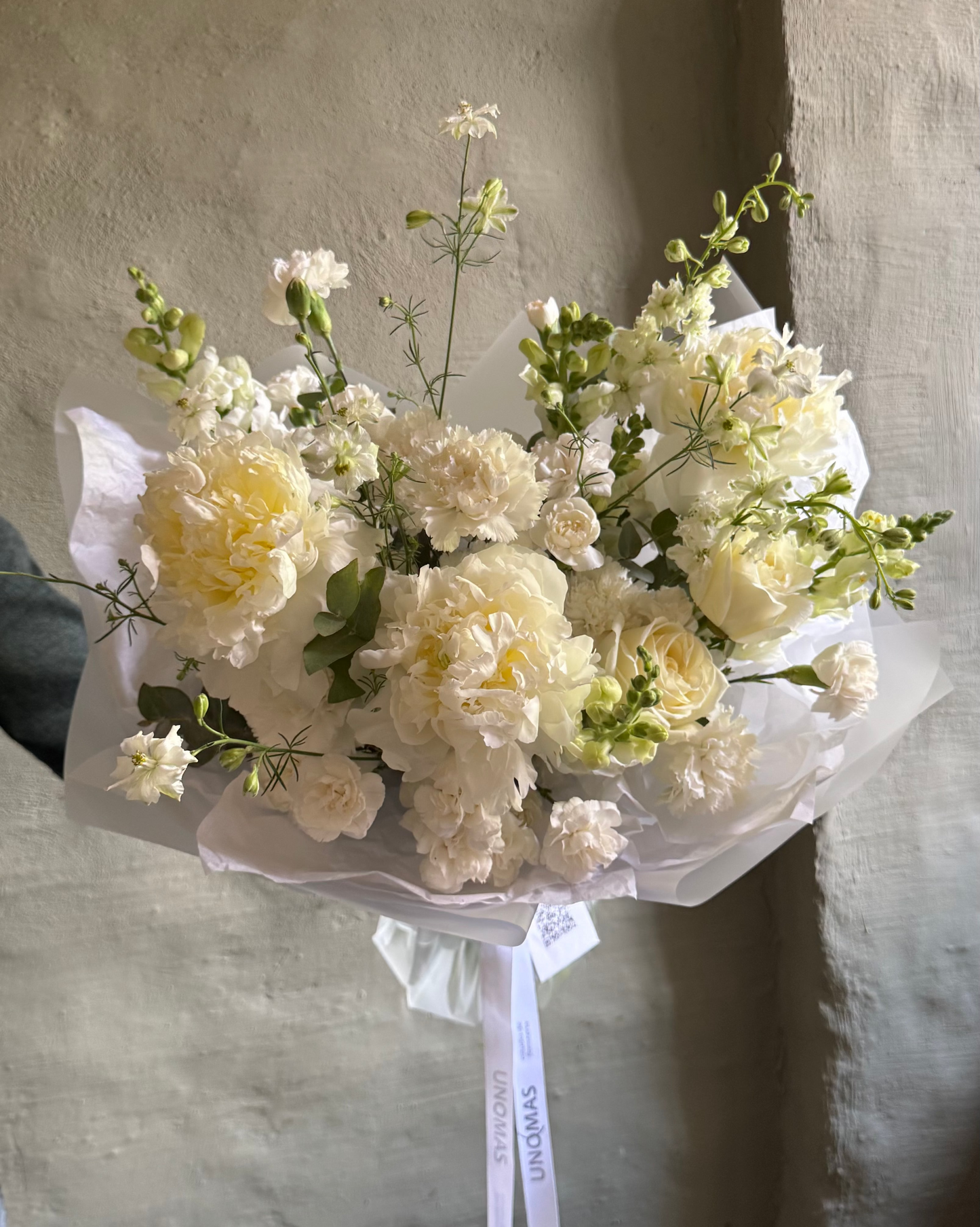 Bouquet of white and yellow flowers peonies with a white ribbon against a textured wall.