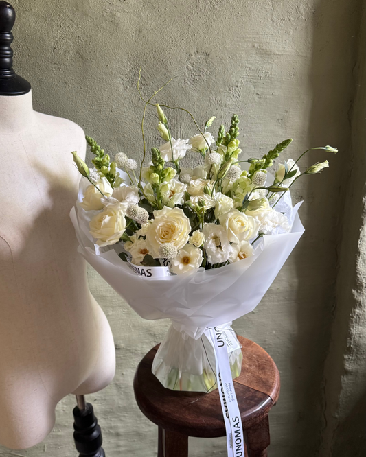 Bouquet of white flowers on a wooden stool next to a mannequin against a textured wall.