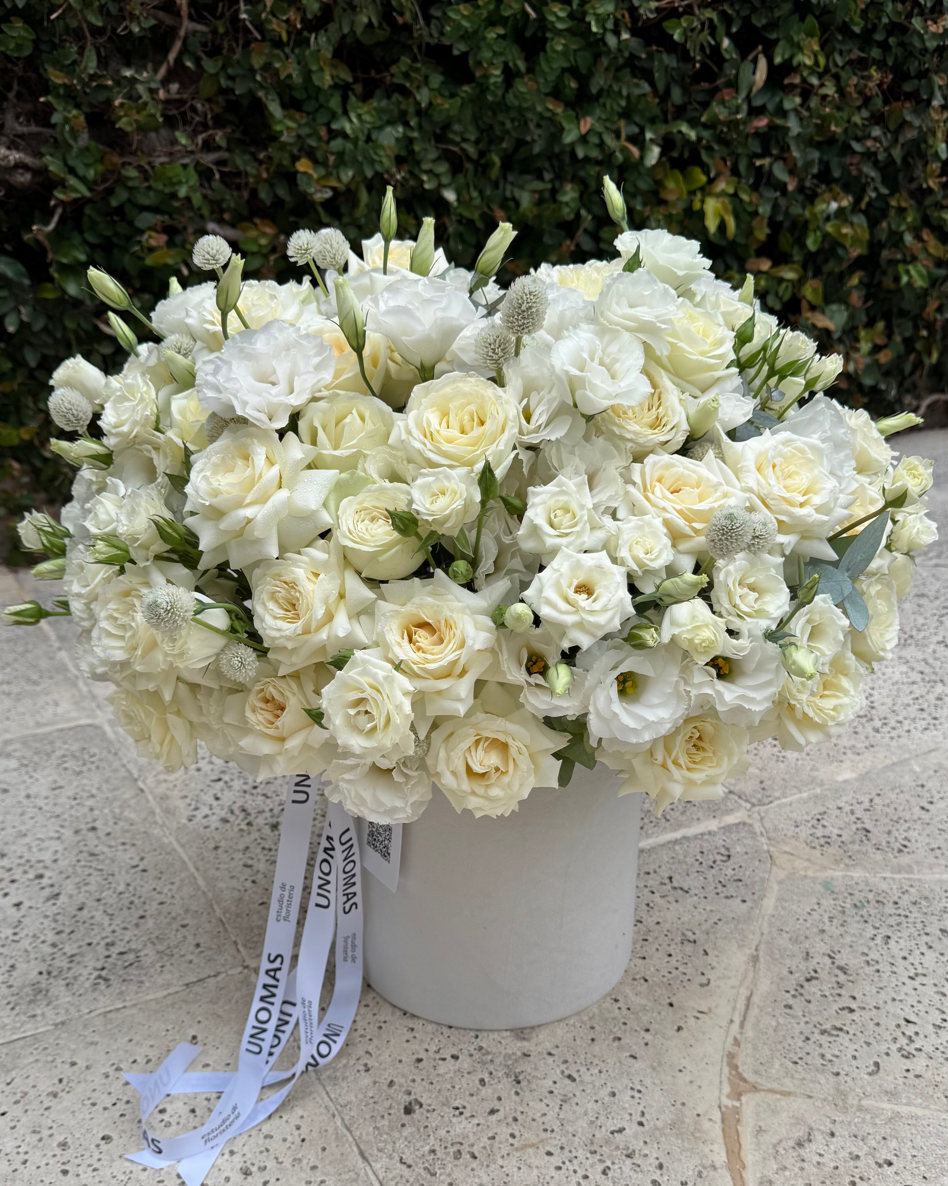 Bouquet of white flowers in a vase on a stone surface with greenery in the background