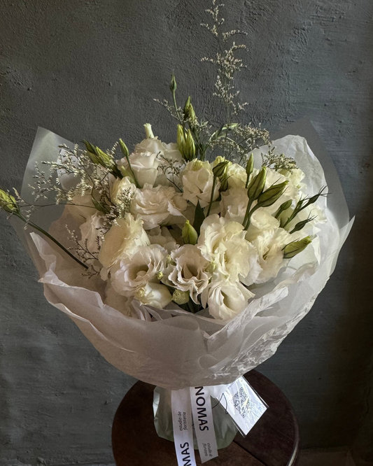 Bouquet of white flowers wrapped in paper with a visible brand label on a dark background