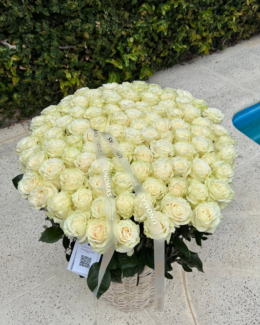Bouquet of white roses in a basket on a stone surface with greenery in the background